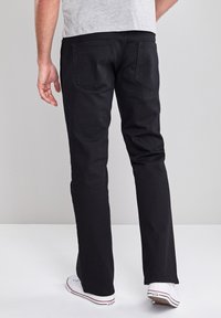 Zwarte denim jeans met een rechte pasvorm, uitgerust met twee achterzakken en een gladde textuur. Gecombineerd met witte sneakers voor een casual uitstraling.