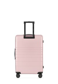 Pink hard-shell suitcase with black retractable handle, side handle, and four black wheels. Vertical ribbed design.
