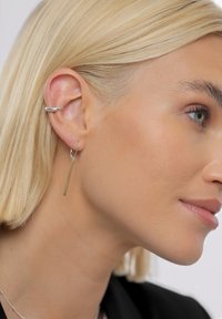 Sølvcreoler og lange, tynde gulddingleøreringe vist på et close-up af et øre og en sideprofil. Glat tekstur og moderne design.