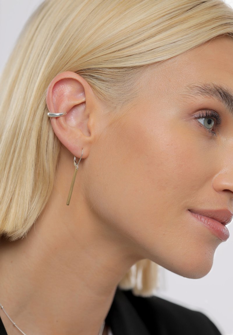 Sølvcreoler og lange, tynde gulddingleøreringe vist på et close-up af et øre og en sideprofil. Glat tekstur og moderne design.