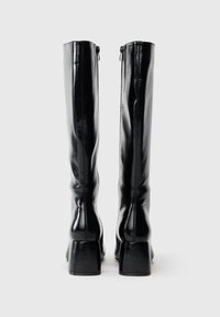 Melnas ādas ceļgala augstās zābaciņas ar elegantu apdari, kvadrātveida papēdi un rāvējslēdzēja detaļu aizmugurē. Gluda tekstūra ar minimālu šuvju skaitu.