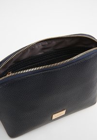 Marineblå tekstureret læderpung med gyldent lynlås, der har en glat inderside og flere rum til organisering.