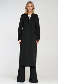 Czarny płaszcz zapinany na podwójne guziki z klapami z wycięciem, dwoma przednimi kieszeniami i teksturowanym materiałem. Szerokie czarne spodnie będące doskonałym uzupełnieniem płaszcza.