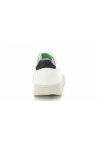 Sneaker bianco con finitura testurizzata, cappuccio del tallone blu navy e suola beige morbida. Dettaglio del logo verde sulla parte interna del tallone. Design minimalista.