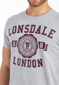 Pilkas medvilnės marškinėliai su bordo spalvos spauda ir emblema, apvaliu autoriaus iškirpimu, trumpomis rankovėmis, išryškintai turi užrašą "Lonsdale London".