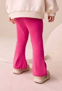 Ribbstickade, rosa utsvängda leggings med vågformade fållar, kombinerade med ljusa sneakers. Mjuk tygstruktur syns i designen.