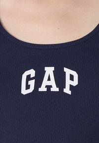 Canotta a coste blu navy con logo "GAP" bianco al centro. Il collo è rotondo con un bordo liscio e rifinito.