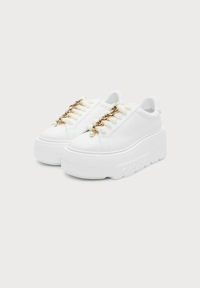 Λευκά sneakers με πάτο πλατφόρμα, χοντρές σόλες και χρυσά κορδόνια με μικρές λευκές χάντρες σε μονόχρωμο φόντο.