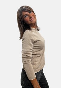 Maglione beige a maglia con maniche lunghe, scollo rotondo e polsini a coste, abbinato a jeans scuri; texture morbida e design casual.