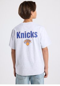 Gray cotton t-shirt featuring "Knicks" in blue letters on the back, with a basketball logo below it. Casual fit, short sleeves, round neckline.
