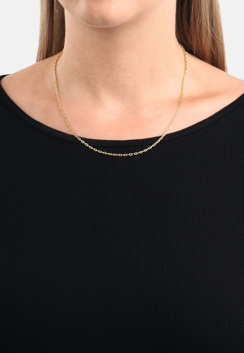 Guldhalsband med sammankopplad oval mönster, vilande på bar hud, buren över en svart ribbad topp med vid nedskärning.