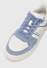 Blue suede sneaker with white leather accents, round toe, perforated toe box, and flat laces. "TOMMY JEANS" logo in blue on the side.