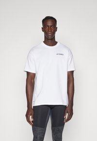 White cotton t-shirt with short sleeves, featuring a small black "TERREX" logo on the upper left chest, paired with black athletic leggings.