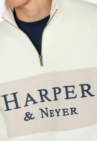 El pulóver de media cremallera de color claro presenta un panel beige con el texto en azul oscuro "HARPER & Neyer", tela suave y hardware de cremallera metálica.