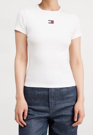 T-shirt blanc côtelé avec un col rond et des manches courtes, arborant un petit logo "TOMMY HILFIGER" rouge, blanc et bleu sur la poitrine.