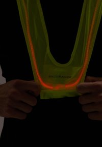 Fluoreszierende gelbe Sicherheitsweste mit roten reflektierenden Akzenten und Netzgewebe, um den Hals getragen. Auf der Vorderseite mit "ENDURANCE" beschriftet.