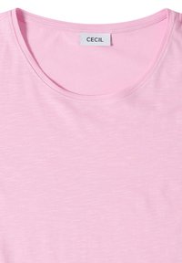 T-shirt rose clair à col rond avec une étiquette blanche au col affichant le nom de la marque "CECIL".