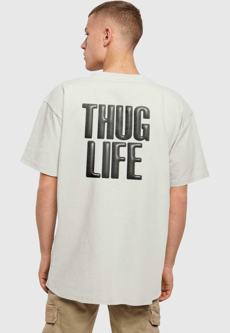 Lys grå oversized t-skjorte med korte ermer, med teksten "THUG LIFE" i fet svart skrift på baksiden. Laget av bomull.