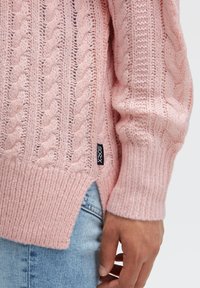 Zopfstrickpullover in zartem Rosa mit gerippten Bündchen und einem seitlichen Schlitz. Enthält ein kleines schwarzes Etikett mit der Aufschrift "SOCX".