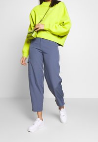 Neongrön sweatshirt med hög krage, matchad med ljusblå, avsmalnande cargobyxor med sidofickor och vita sneakers.