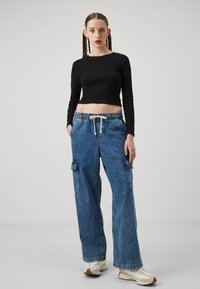 Top negro de manga larga recortado combinado con pantalones cargo anchos de mezclilla azul con grandes bolsillos laterales y cintura con cordón.