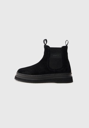 Svarta mocka chelsea boots med elastiska sidopaneler, dragflikar och en texturerad gummisula. Ligger något upphöjd plattform med sömdetaljer.