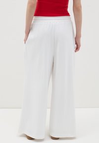 Pantalones anchos blancos con una textura suave y cintura elástica. Bolsillos visibles a los lados, sin patrones ni acentos distintos.