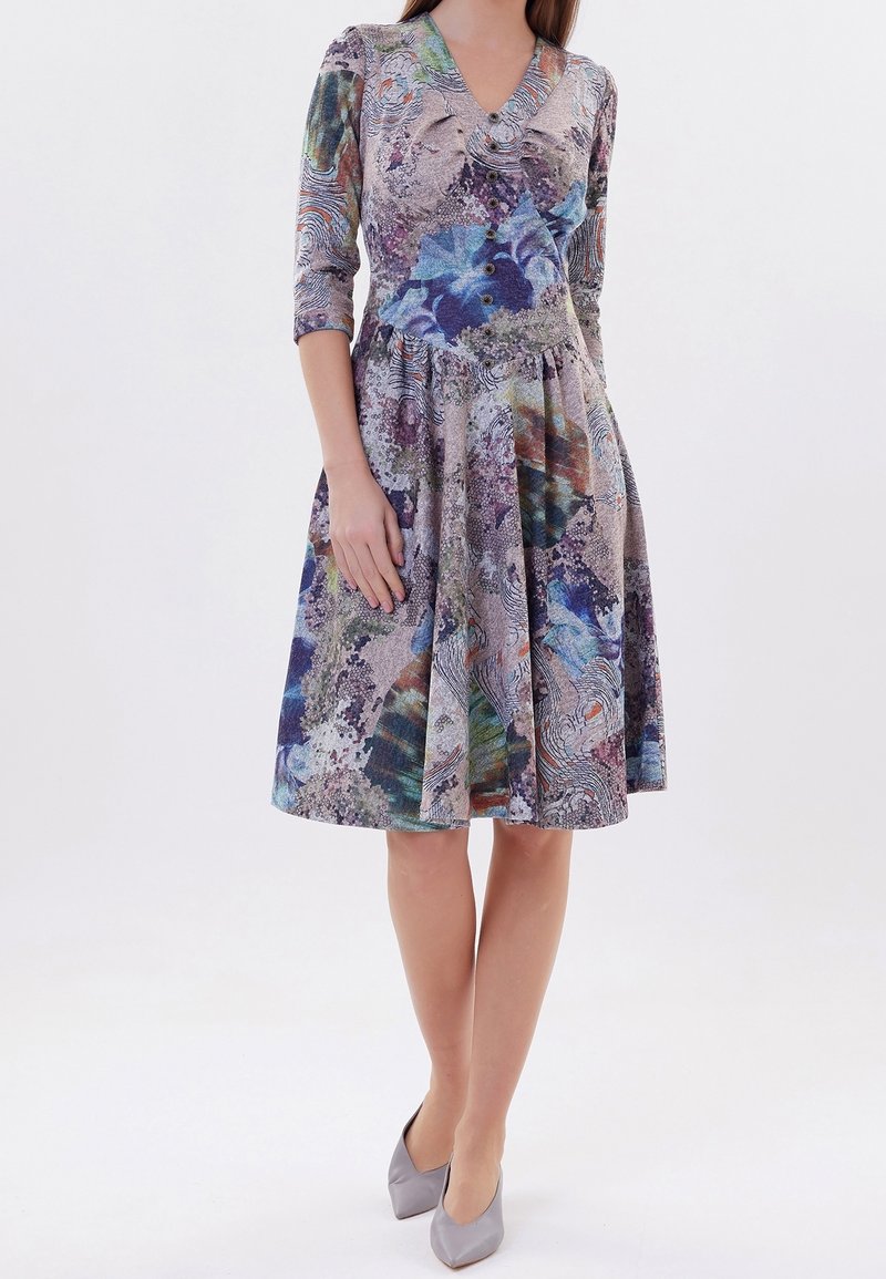 Robe imprimée avec un col en V, des manches trois-quarts et une jupe évasée dans plusieurs couleurs, présentant un motif texturé et des accents de boutons.