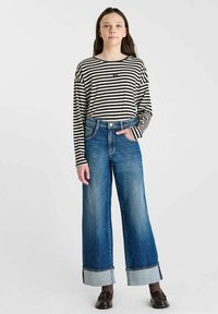 Chemise rayée à manches longues en noir et blanc, associée à un jean en denim bleu à jambes larges avec un ourlet retroussé. Détails comprenant des poches avant.