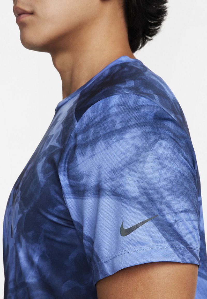 T-shirt de sport bleu avec un motif marbré, manches courtes, col rond et un logo Nike noir sur l'épaule gauche. Tissu texturé.