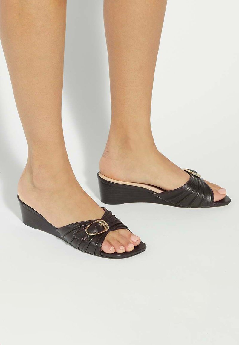 Black leather wedge sandals with a wide, pleated strap and gold buckle detail. Open toe design, with smooth texture and low heel.