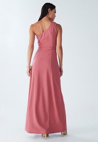 Abito lungo monospalla in tessuto rosa chiaro. Texture liscia, vita aderente, gonna leggermente svasata, dettagli sottili di drappeggio.