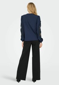 Blusa navy con maniche a palloncino, con dettagli in pizzo nero intricati sulle maniche. Abbinata a pantaloni neri a gamba larga e tacchi.