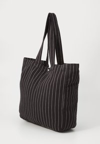 Bolso tote a rayas negras hecho de tela, con rayas blancas horizontales, dos asas resistentes y una forma rectangular amplia.