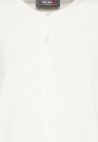 Biała kardigan z dzianiny z okrągłym dekoltem, pięcioma guzikami z przodu i miękką teksturą. Metka brzmi "MOS MOSH."