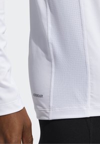 Vit långärmad träningstop med texturerad sidopanel, logotyp "AEROREADY" nära nederkanten, lättviktsmaterial och ventilerad design.