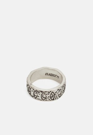Anel de prata com uma forma hexagonal, apresentando padrões e acentos gravados. No interior, marcado com "CLASSIC '77." Textura suave, acabamento polido.