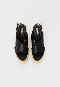 Sorte lær sandaler med kryssreimer, som har en jute kile såle. Innsiden viser en logo på en glatt overflate.