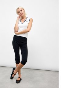 White sleeveless top with navy V-neck trim and embroidered detail, paired with black cropped leggings and black mesh shoes.