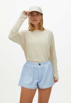 Lichtbeige langemouwen shirt met subtiele branding, gecombineerd met zachte, lichtblauwe shorts met een elastische tailleband en koord.