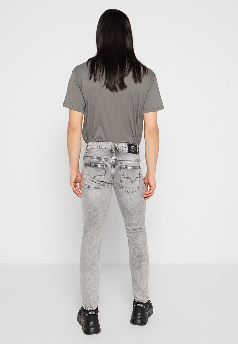 T-shirt grigia a maniche corte, abbinata a jeans skinny grigi chiari con finitura sbiadita e tasche posteriori. Scarpe nere completano l'outfit.