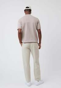 T-shirt en maille à manches courtes de couleur rose clair, avec un motif en zigzag texturé, associé à un pantalon beige clair ample et des baskets blanches.