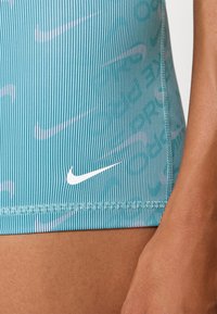 Lyseblå stripete svømmebukser med en subtil Nike-logo i hvitt. Stoffet har en glatt tekstur og har et mønstrete design.