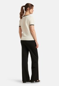 Witte textuur short-sleeve top met zwarte afwerking, gecombineerd met zwarte wijde broekspijpen. Focus op eenvoudige lijnen en een ontspannen silhouet.