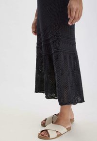 Abito nero in maglia con texture a trama aperta e orlo decorato, abbinato a sandali leggeri beige con incrocio su suola di sughero.