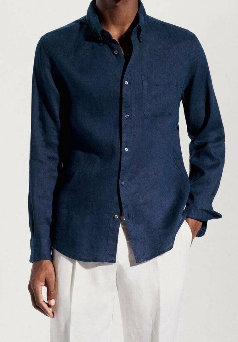 Chemise bleu marine à boutons, en tissu texturé, dotée d'une poche plaquée, de manches longues et de boutons blancs. Associée à un pantalon de couleur claire.