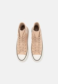 Zapatillas altas de lona beige claro con punteras de goma blanca, ribete negro y cordones planos. Presentan un parche de logo en el lateral.