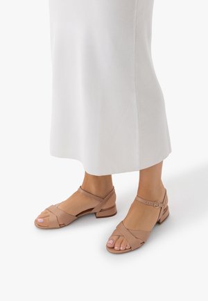 Picioare purtând sandale nud cu toc mic, cu bretele la gleznă și bretele încrucișate în față, asortate cu o fustă albă până la gleznă.