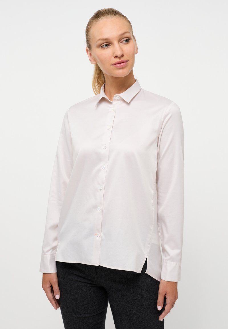 Blusa rosa chiaro a maniche lunghe con collo a camicia, chiusura a bottoni e spacchi laterali. Tessuto liscio e lucido con design slanciato.