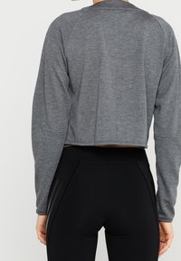 Grå kortärmad sportjacka med texturerad tyg och raglanärmar, kombinerad med höga svarta leggings med tre ränder.